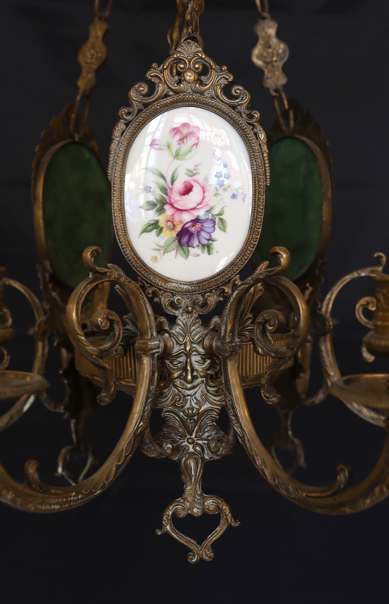 A 1930s English bronze and porcelain six light chandelier with central foliate stem and three oval porcelain plaque decorated with flowers, height 79cm. width 55cm